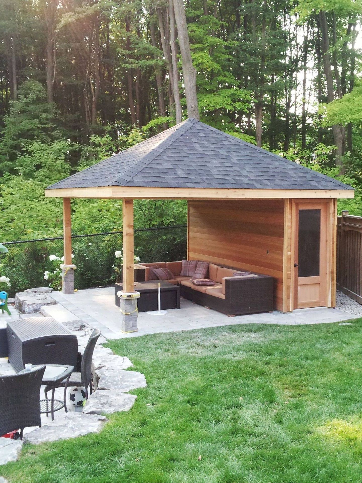 Outdoor lounge with a brown sectional, under a gazebo with a dark roof.
