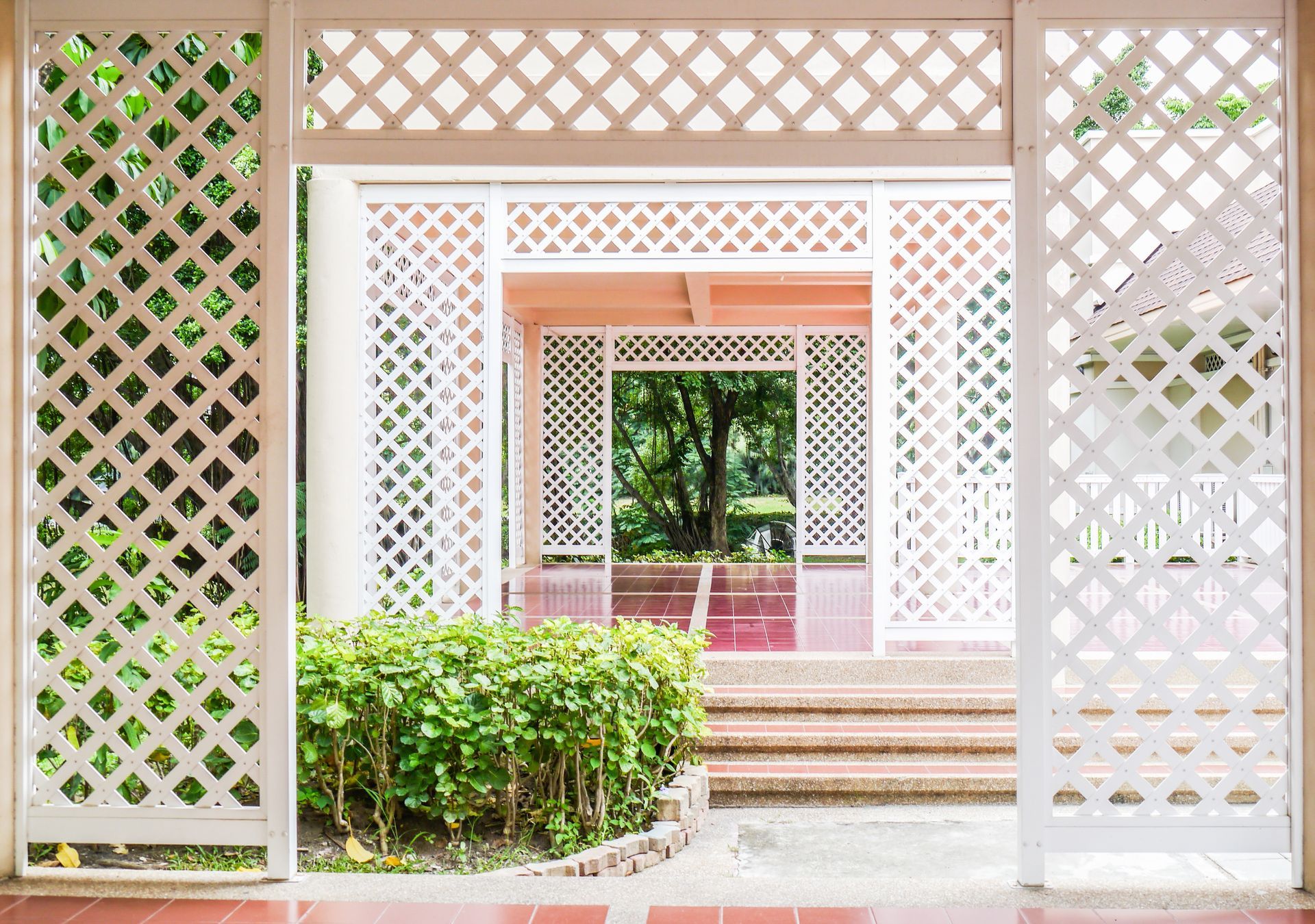 White latticework frames a garden pathway, leading to a structure with visible trees.