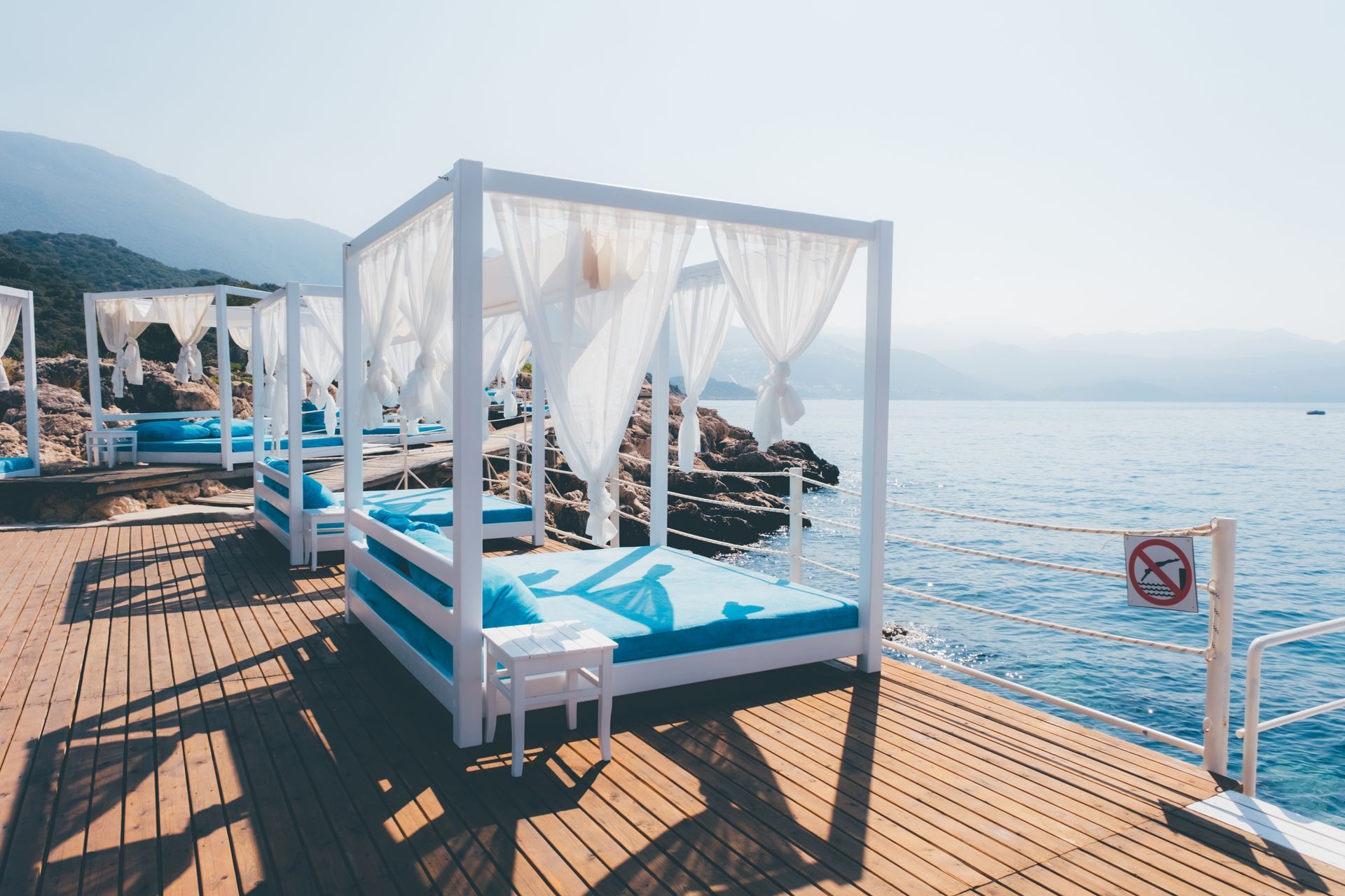 Wooden deck with white cabanas, blue cushions, overlooking the sea.