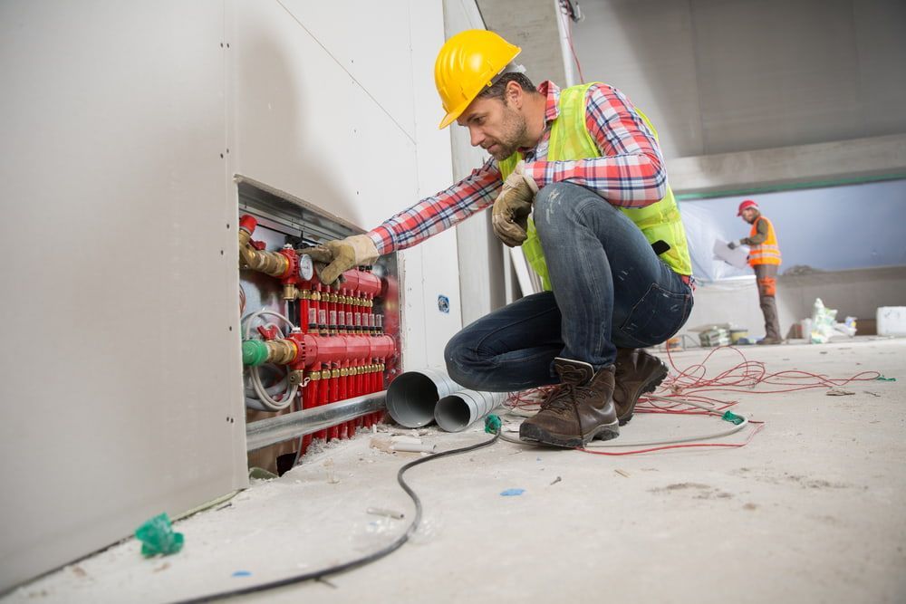 A Construction Worker Is Kneeling Down to Fix a Pipe — Danzair Refrigeration & Airconditioning in Lismore, NSW