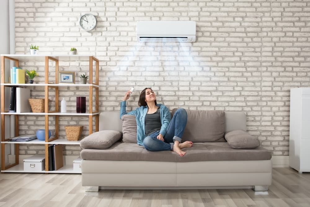 A Woman Is Sitting on A Couch Under an Air Conditioner — Danzair Refrigeration & Airconditioning in Lismore, NSW