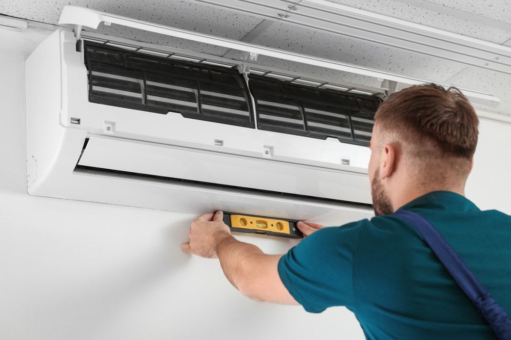 A Man Is Installing an Air Conditioner on A Wall — Danzair Refrigeration & Airconditioning in South Lismore, NSW
