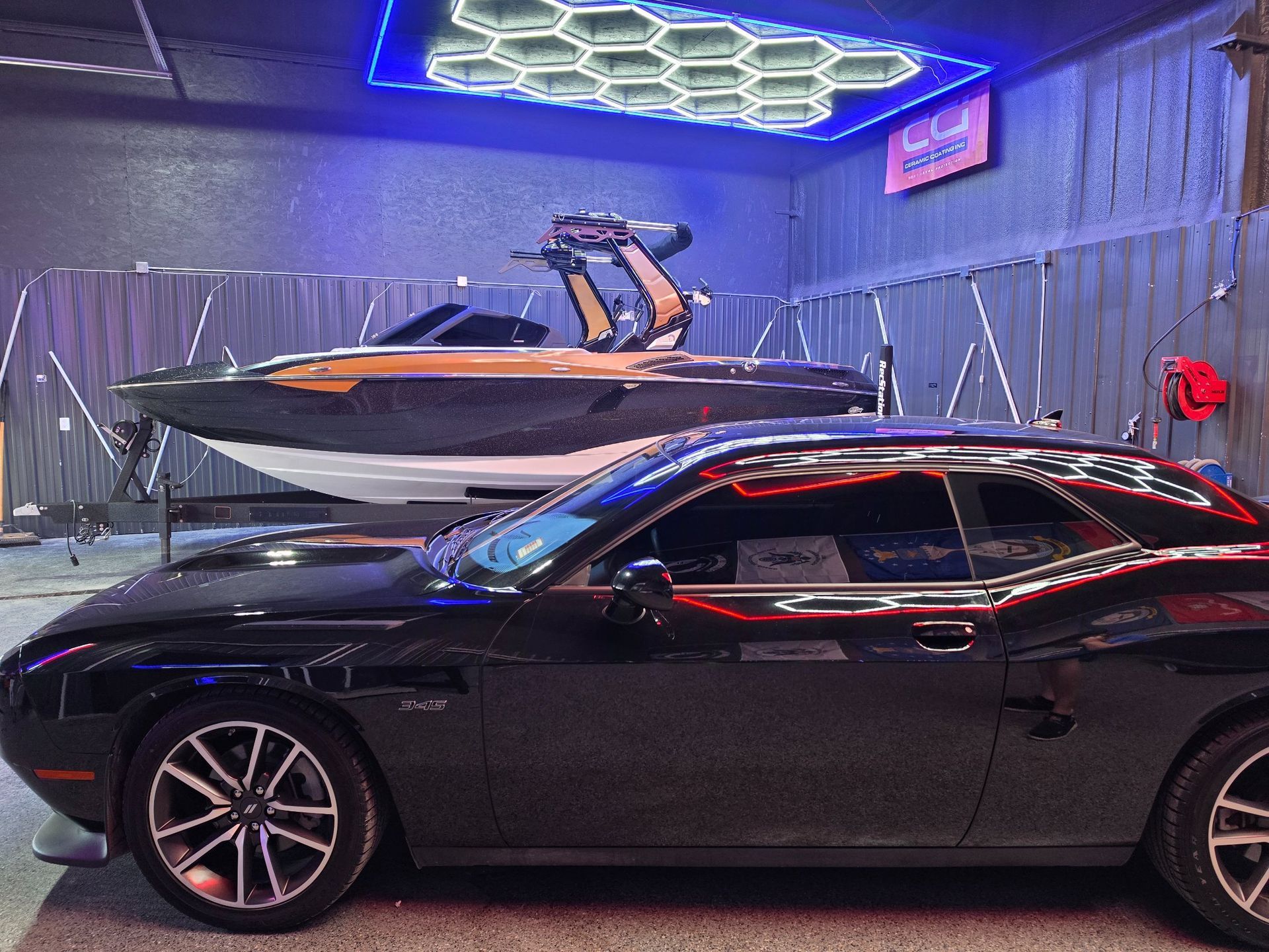 Black car parked beside a white-and-black speedboat inside a showroom with blue neon lighting