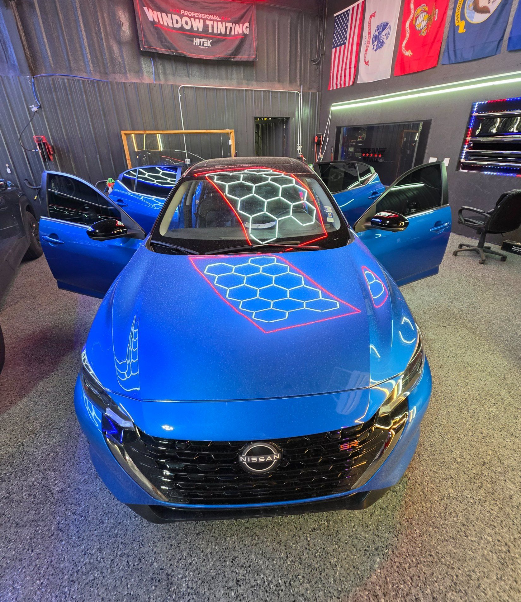 Blue sports car with open doors in a showroom under red hexagonal ceiling lights