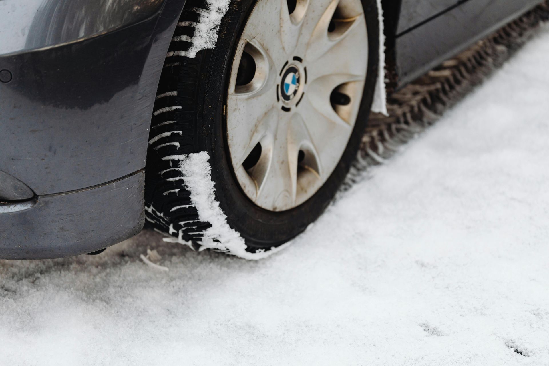 A gray car tire covered in snow on a snowy surface. BMW logo visible on the hubcap.