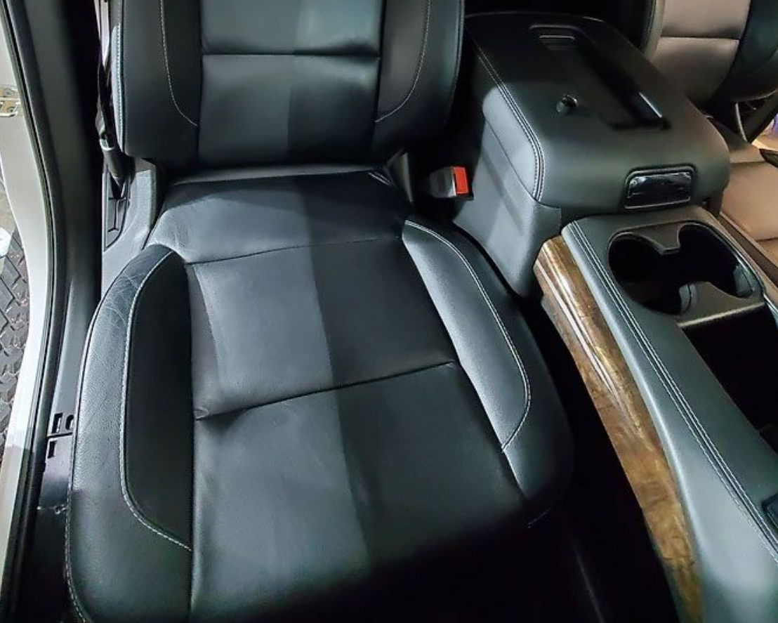 Black leather car seat with a cleaned section, center console, and cup holders.