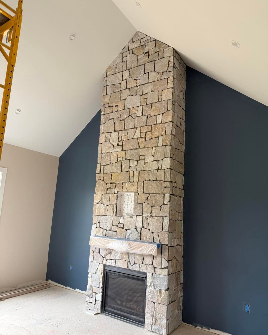 Stone fireplace with a tall chimney in a room with dark blue walls and a vaulted white ceiling