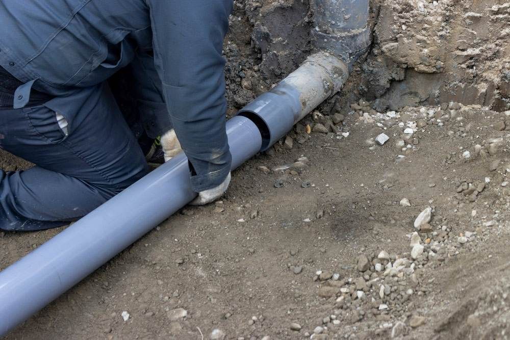 A Man is Working on a Pipe in the Dirt — Treatwater & Plumbing Pty Ltd in North Mackay, QLD