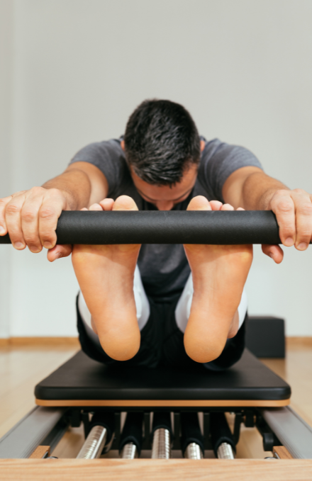 A man is stretching his legs on a pilates machine during an individual training session.
