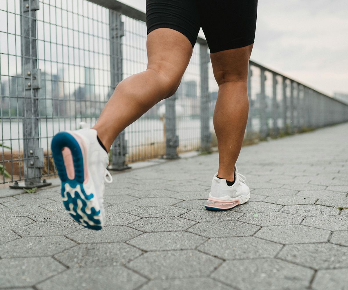 Person running on a paved path wearing white sneakers, fence and water in background.