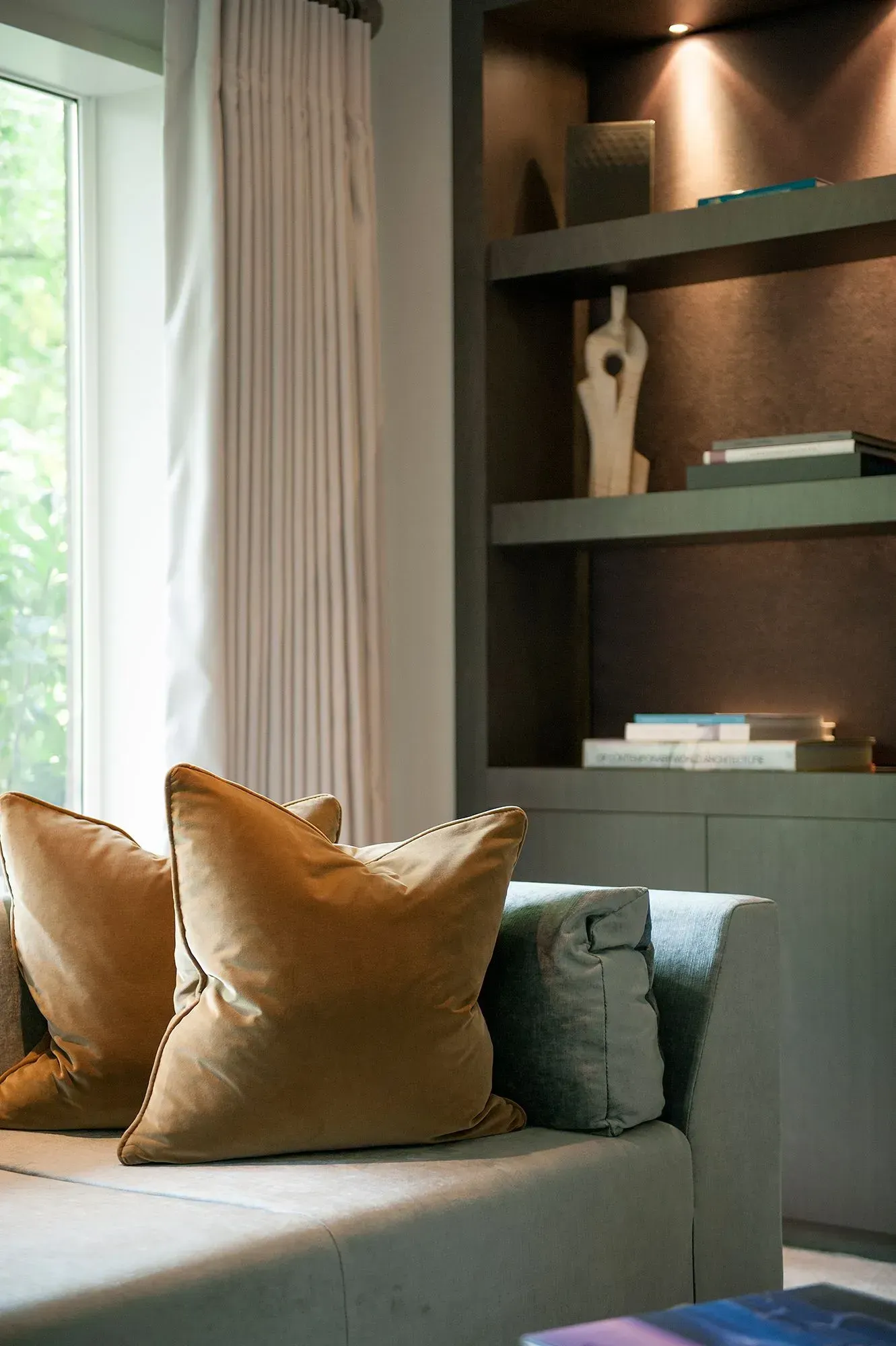 a couch with two pillows on it in a living room next to a window 