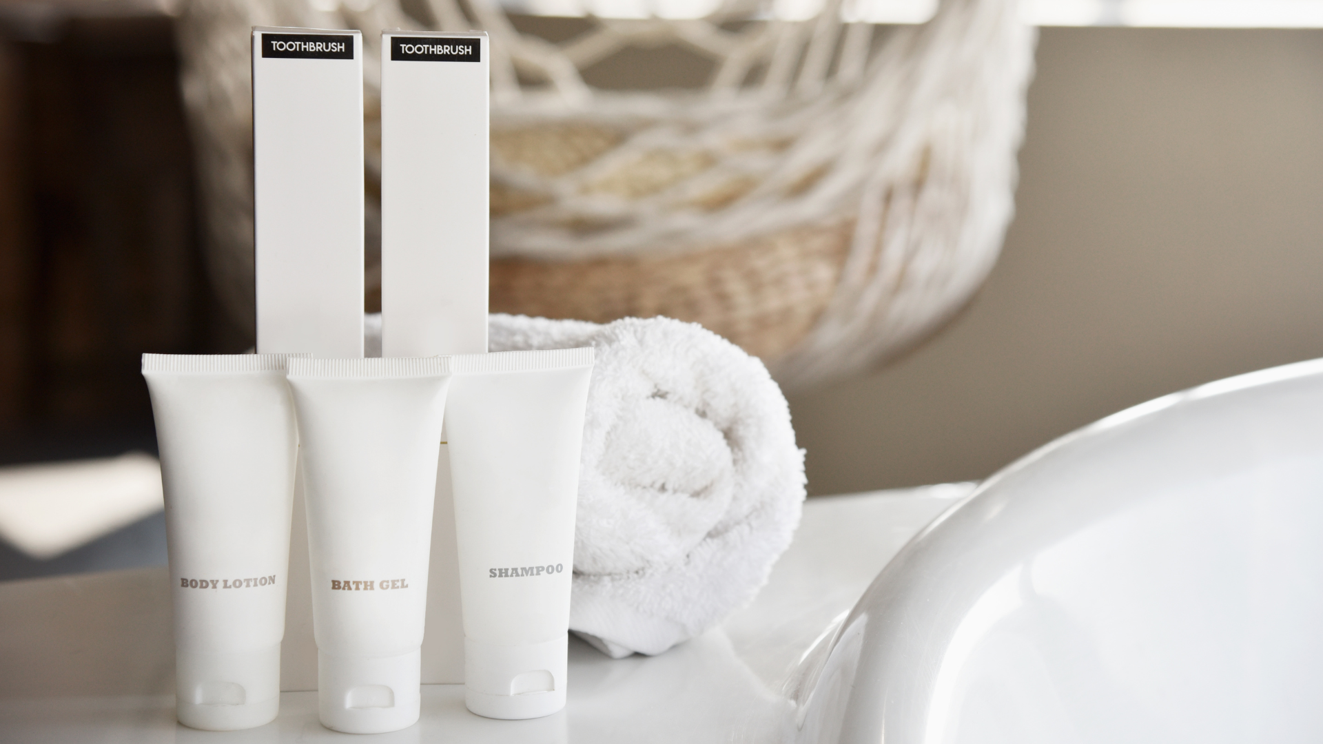 White toiletries and rolled towel on a bathroom counter.