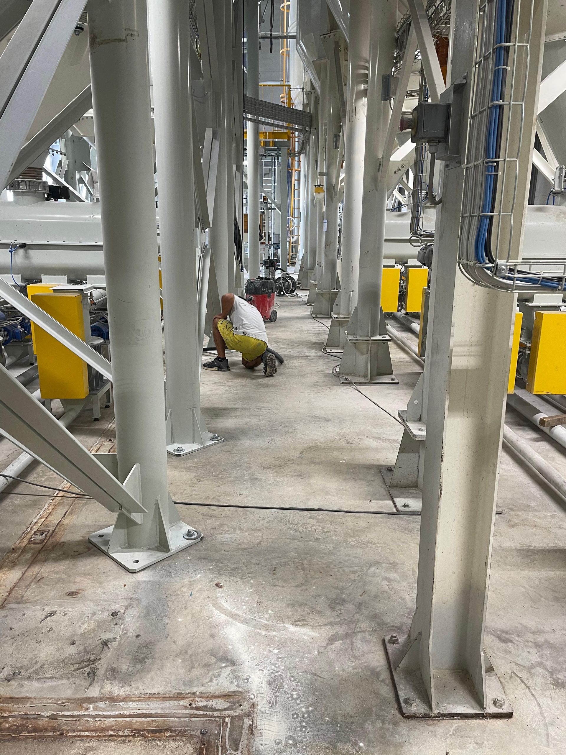 Un operaio con la tuta gialla è inginocchiato tra le travi di sostegno metalliche, all'interno di uno stabilimento industriale.