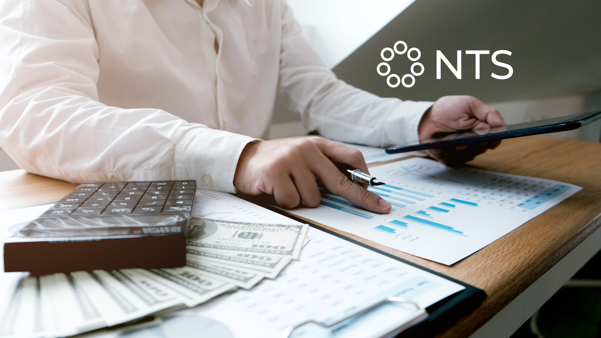 Person in white shirt reviewing financial charts and cash with a calculator on a desk