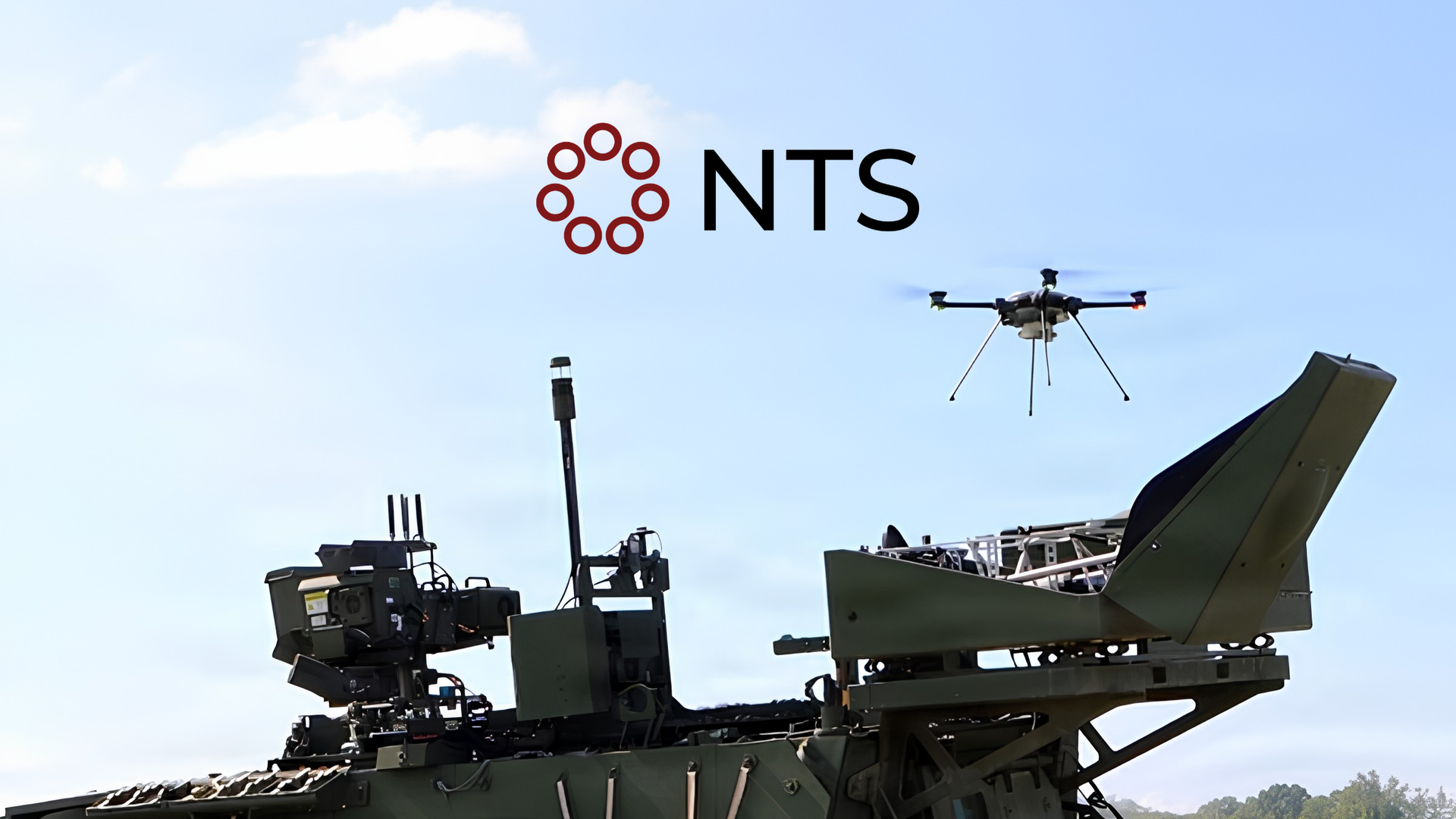 Military drone above armored vehicle with NTS logo against a blue sky