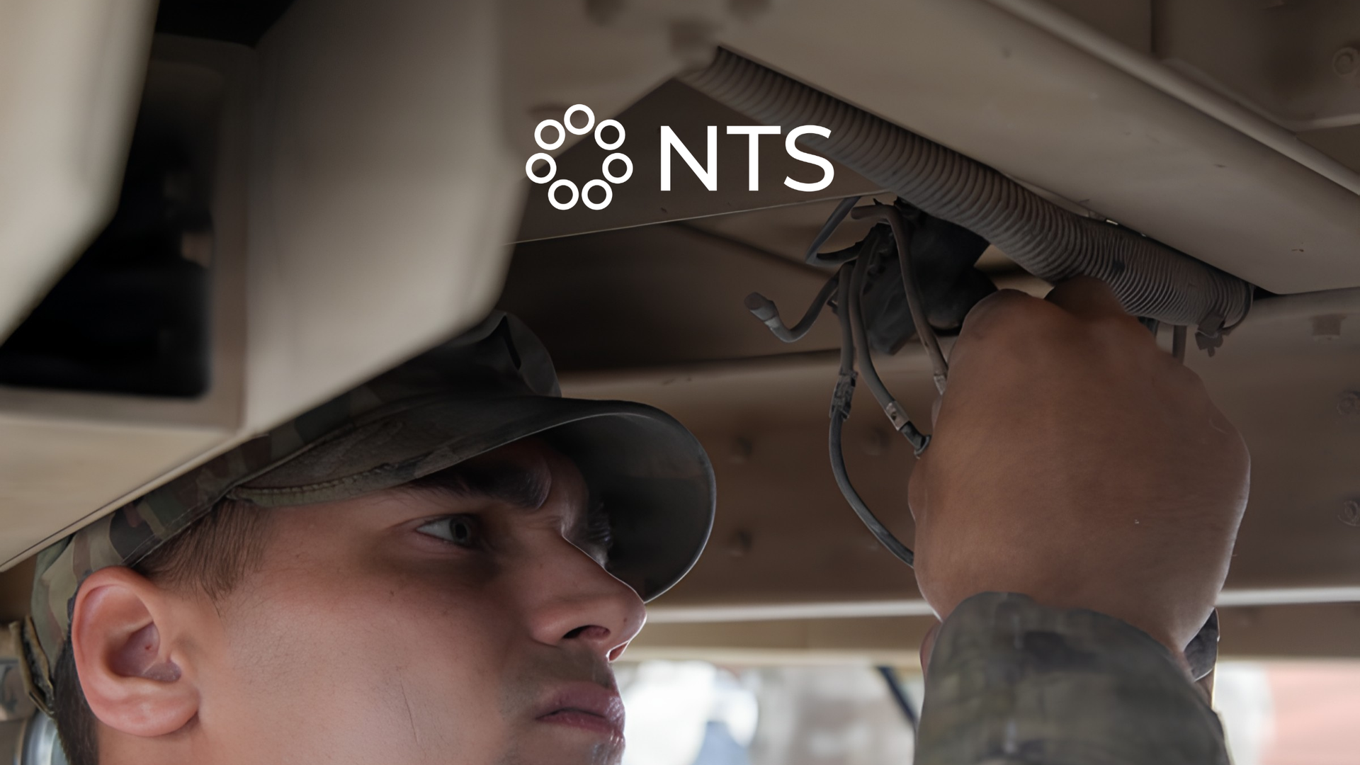 A person in a cap works under a vehicle, adjusting wiring near the dashboard.
