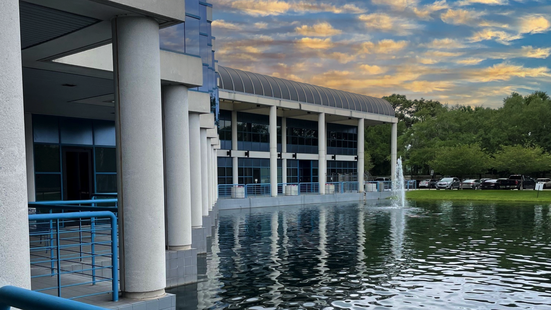 Modern building with blue columns beside a calm reflecting pond at sunset
