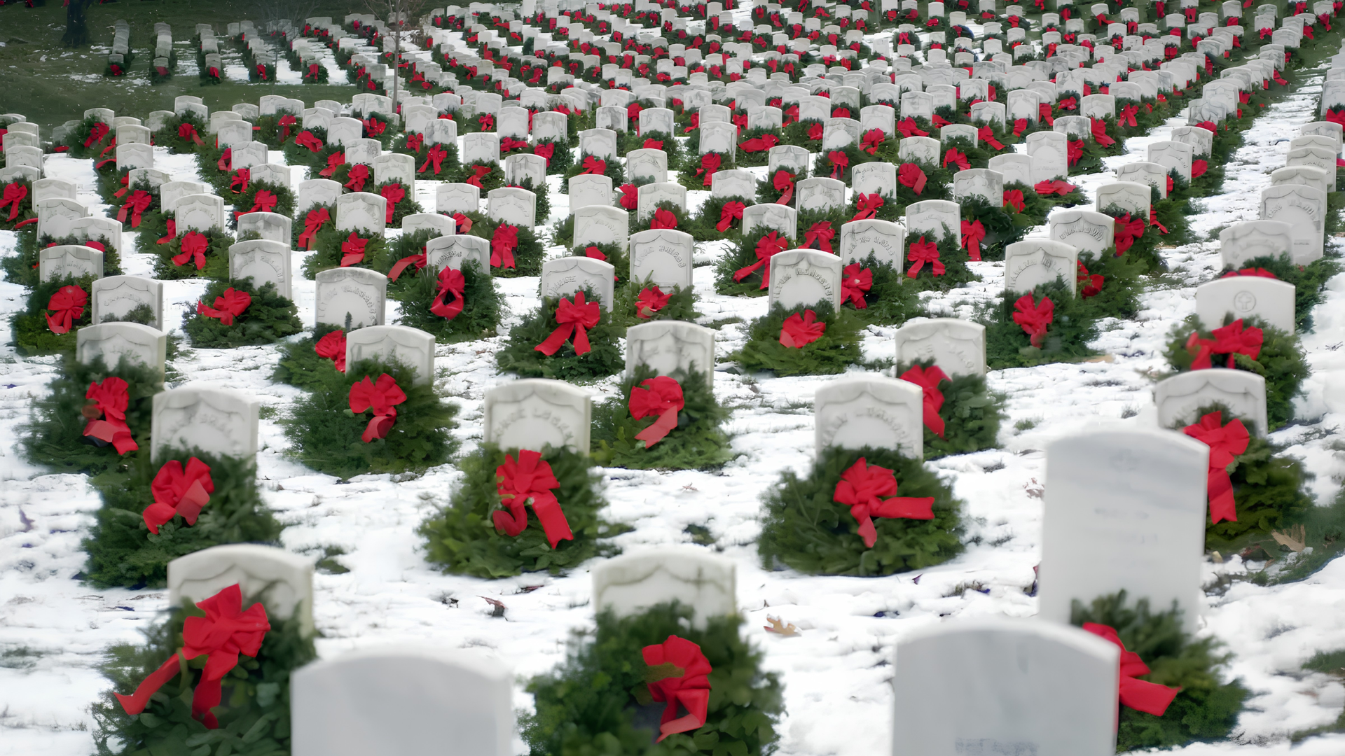 Rows of white gravestones in snow, each decorated with red wreaths.