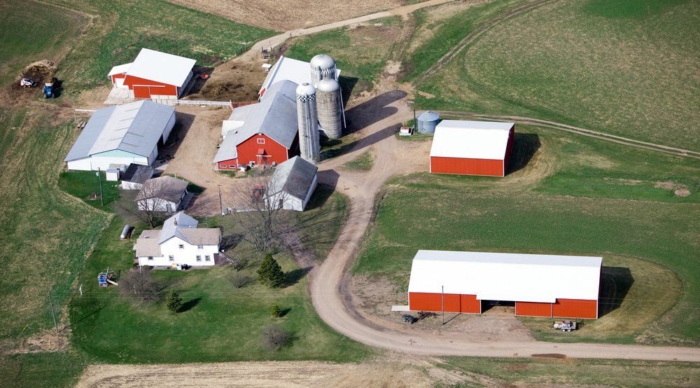 Aerial view of a farm with red and white barns, silos, and a white house, surrounded by green fields.