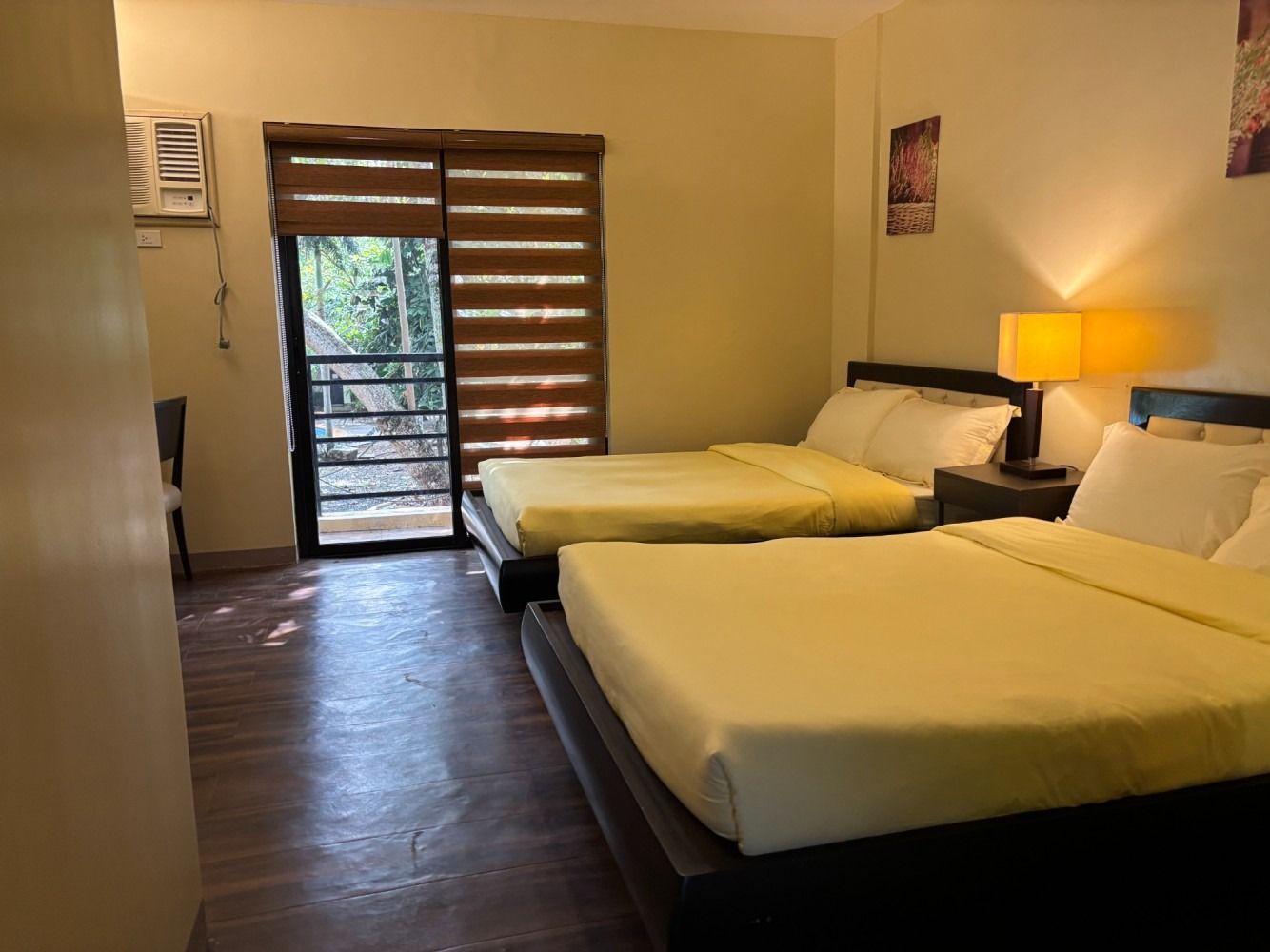 A hotel room with two double beds, yellow sheets, and a door leading to a balcony.