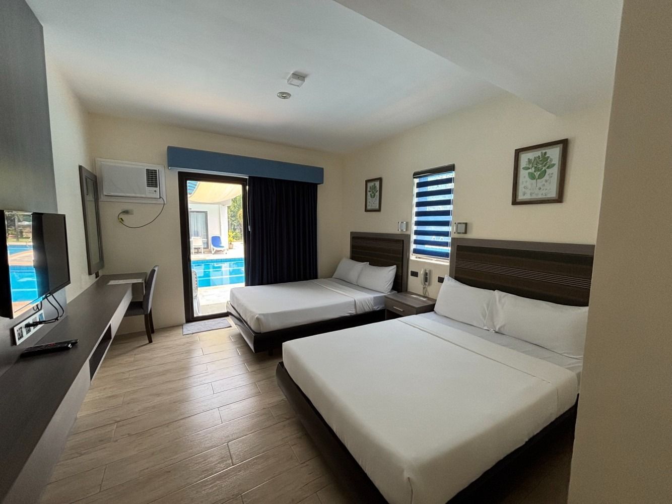 Hotel room with two beds, desk, and a view of a swimming pool.