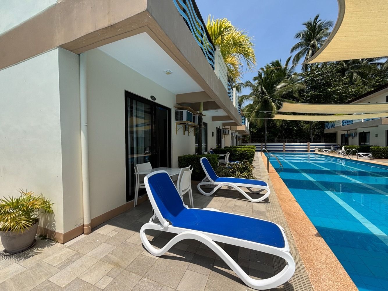 Blue lounge chairs beside a pool on a sunny patio with resort buildings in the background.