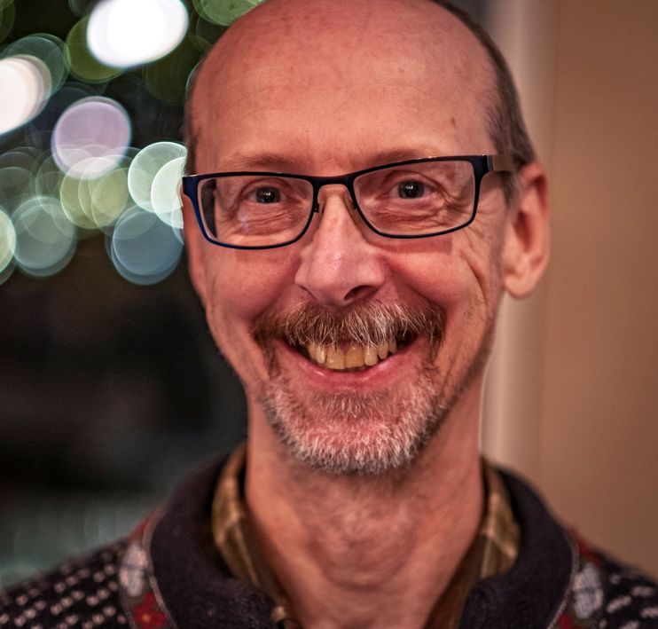En skaldet mand med skæg og briller smiler til kameraet.