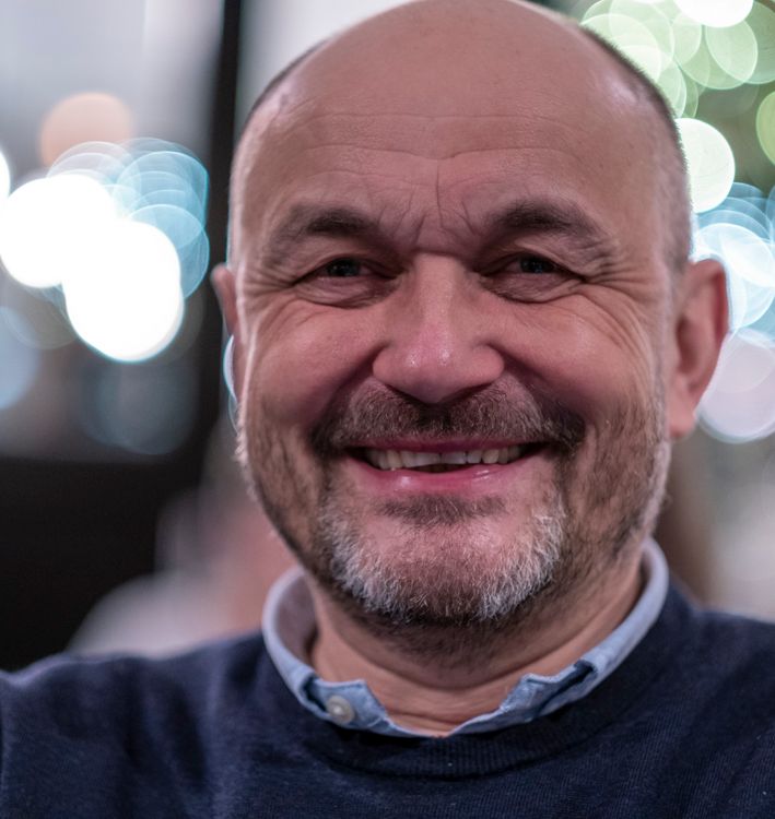 En skaldet mand med briller og skæg smiler på et sort-hvidt foto.