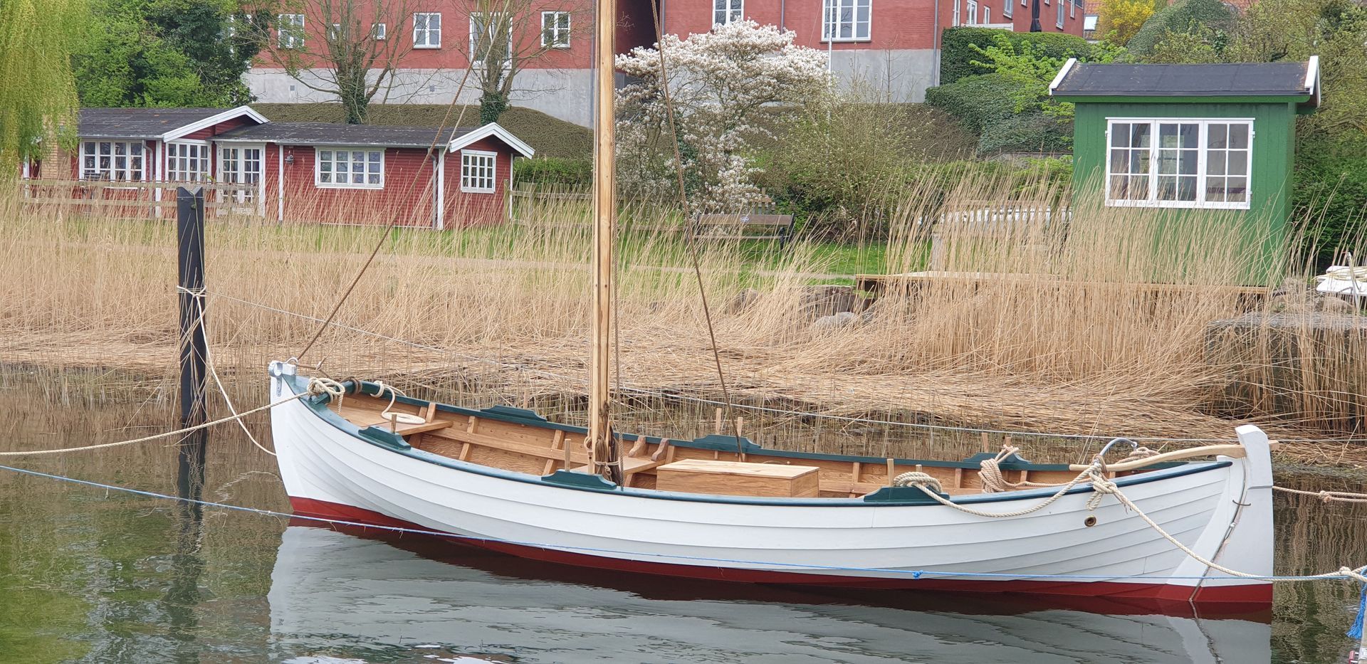 En båd ligger fortøjet i et vandområde med et hus i baggrunden