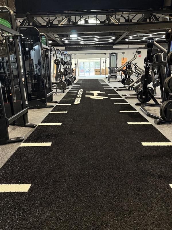 Modern gym interior with a black turf lane, strength machines, and overhead lighting
