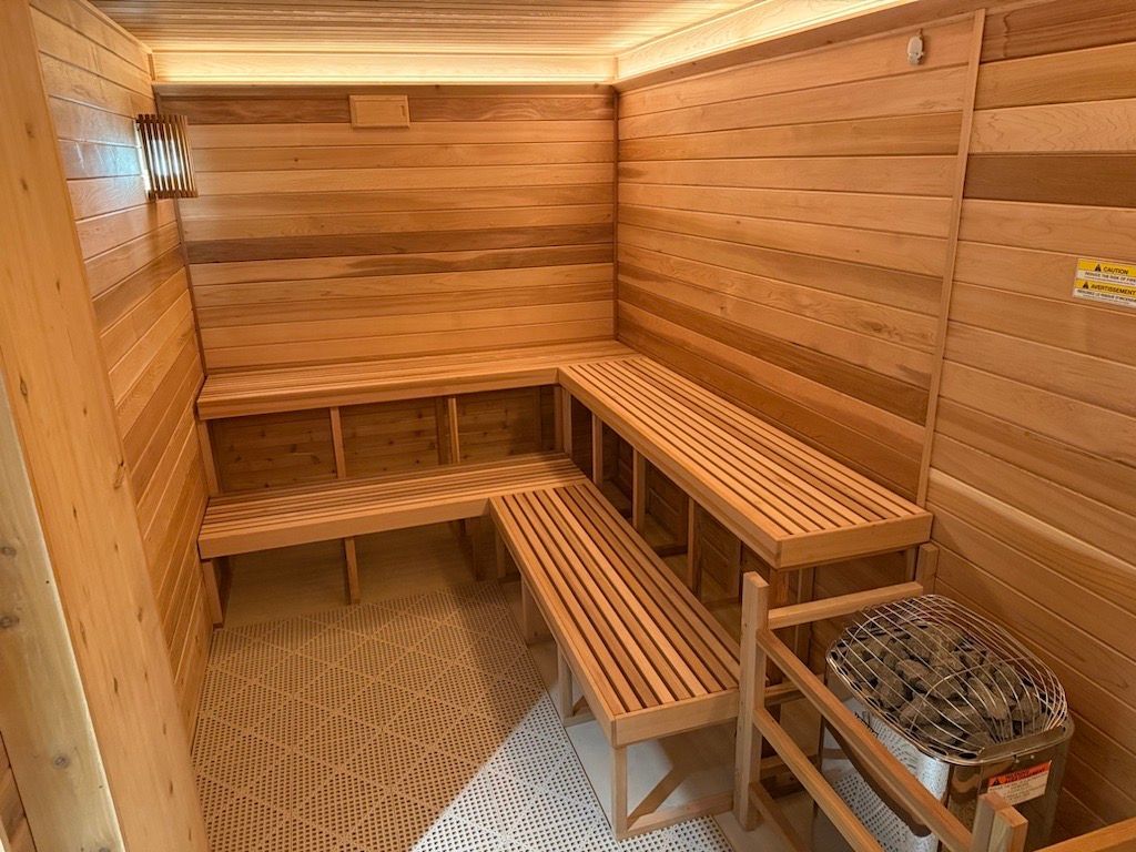 Wood-paneled sauna with L-shaped wooden benches and a heater with stones on the right.