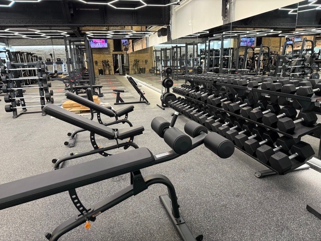 Modern gym with dumbbells, benches, and mirrors under bright ceiling lights