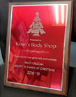 Plaque on a wooden frame with red background, a Christmas tree design, and text for Keen's Body Shop for their generosity.