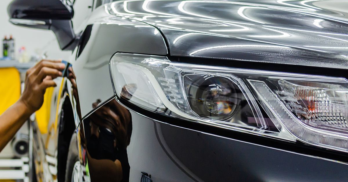A close up of the hood of a car with clouds reflected in the windshield.