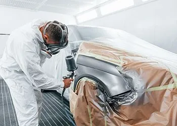 A man is painting a car in a paint booth.
