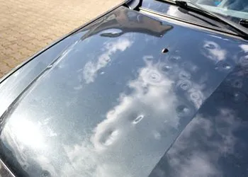 A close up of the hood of a car with clouds reflected in the windshield.
