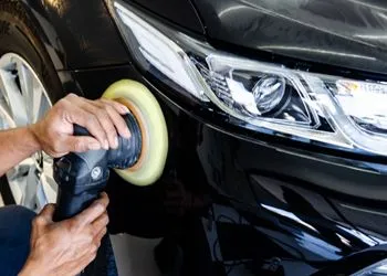 A man is polishing a black car with a polisher.