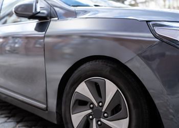 Gray car's front side, showing a wheel and body panel with reflections.