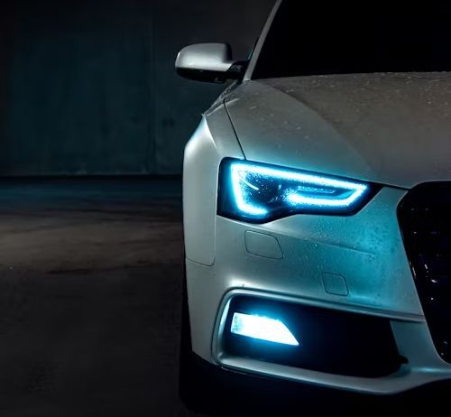 White car with blue headlights in a dark, concrete garage.
