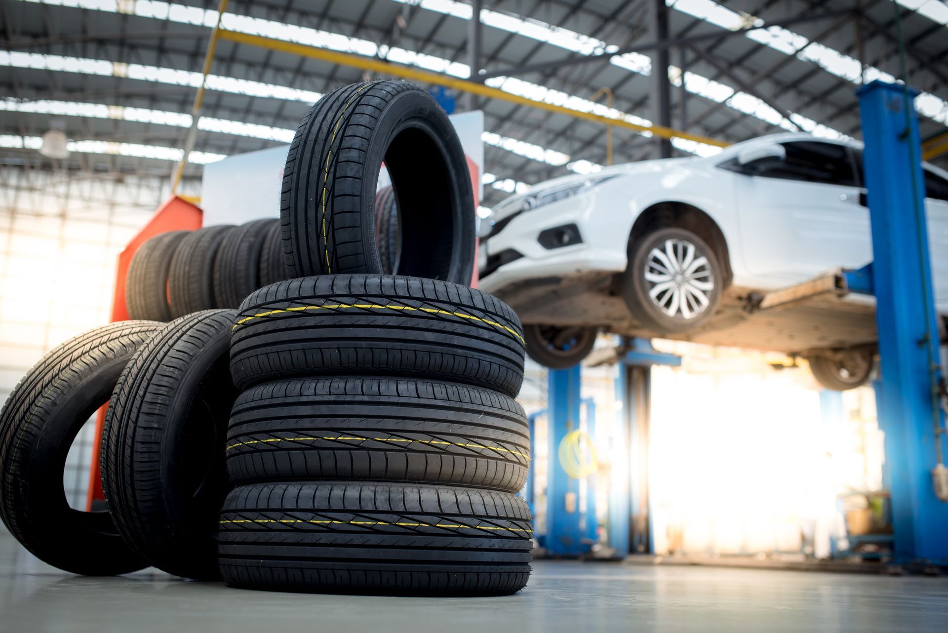 Une pile de pneus dans un garage avec une voiture en arrière-plan.