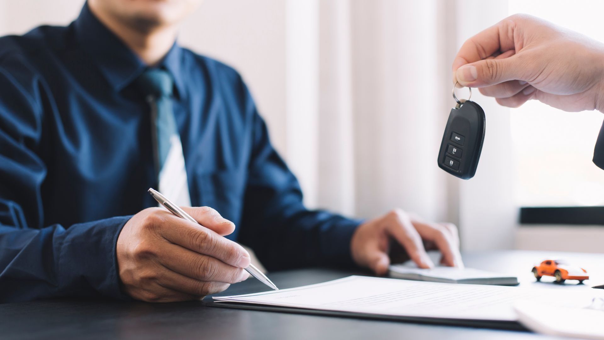 Un homme signe un contrat de location de voiture tandis qu'un autre homme tient une clé de voiture.