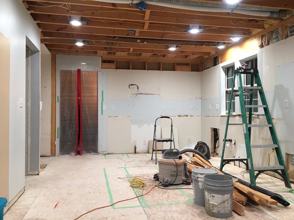 A partially renovated bathroom with a white vanity, exposed wall studs in the background, and a broom on the floor.