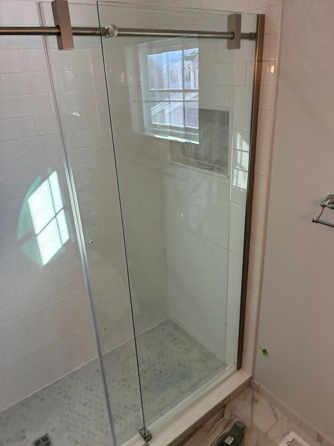 A modern glass shower door with a metal sliding track, installed against white subway tile walls.