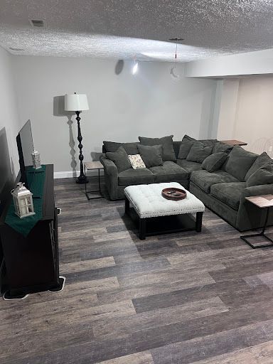 A modern basement living room with a large gray sectional sofa, white tufted ottoman, and a tall floor lamp.