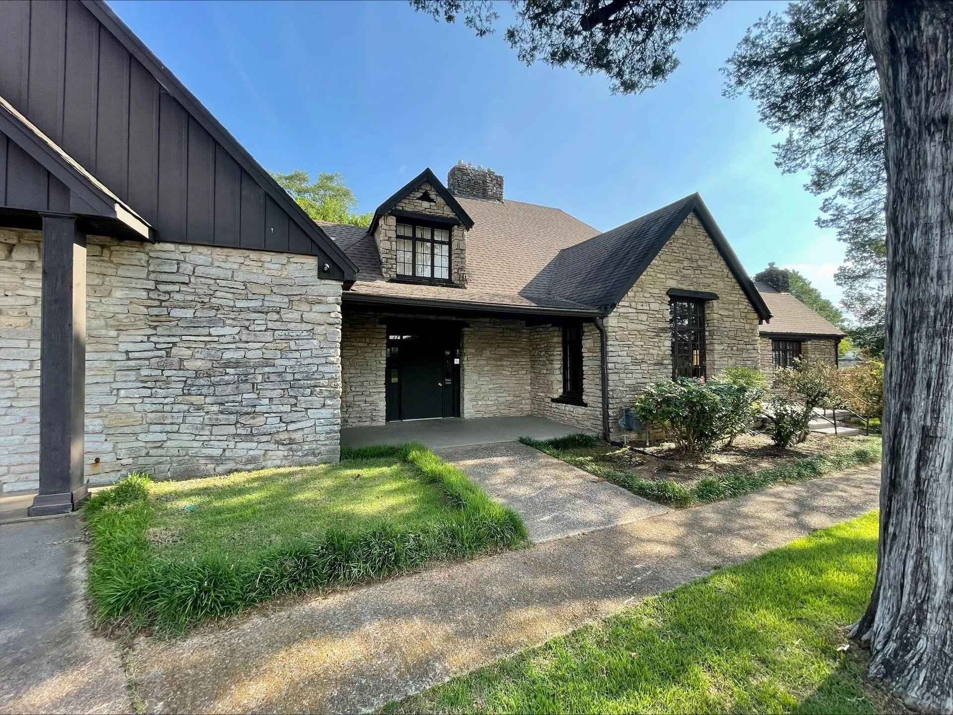 Stone house exterior with a covered entry, dormer window, and front lawn under a blue sky