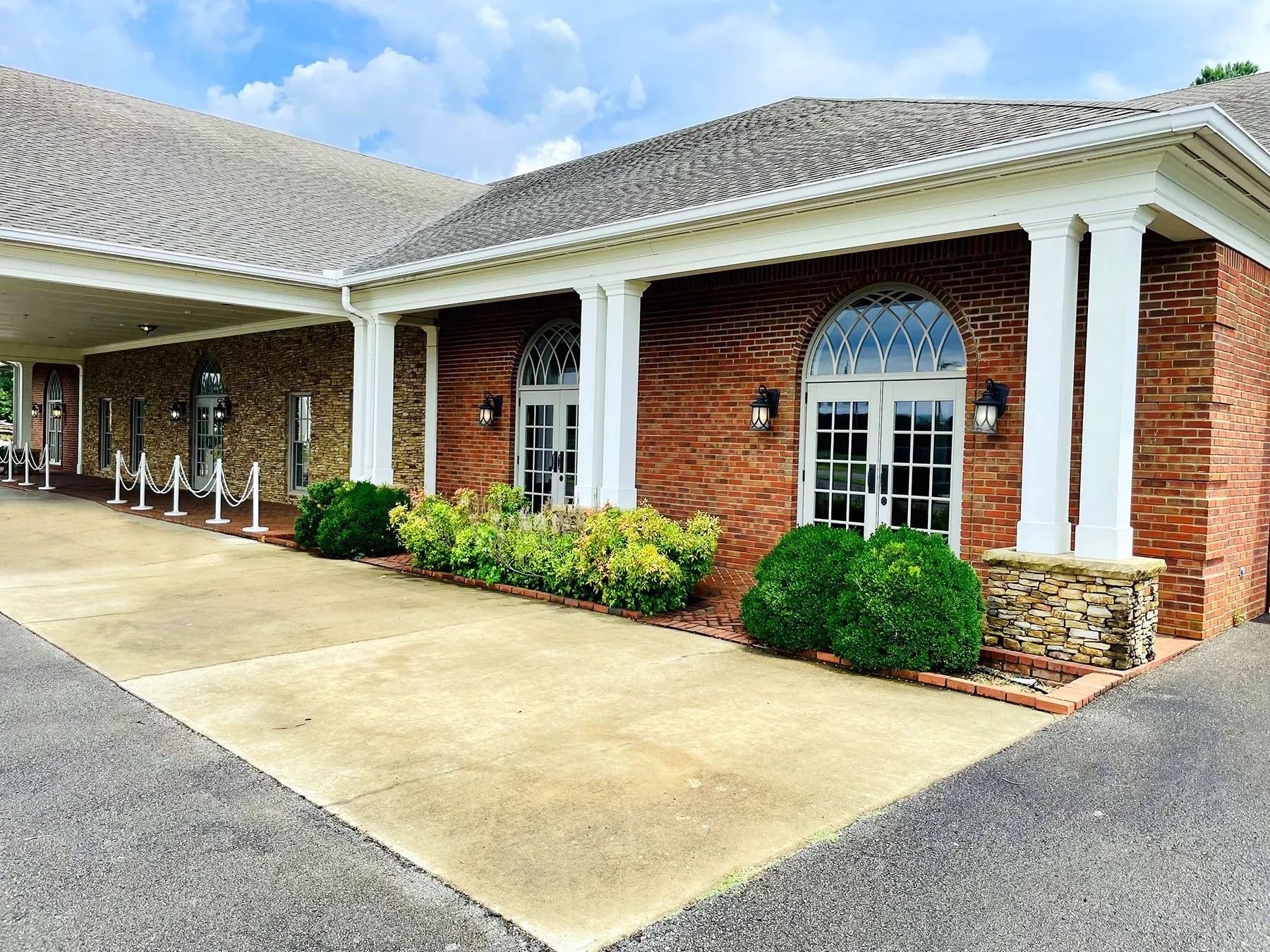 Brick building exterior with white columns, arched windows, and a concrete walkway under a cloudy sky