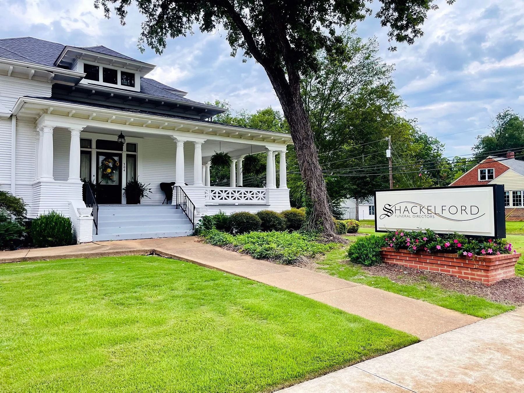Historic white house with porch and sign amid green lawn and trees