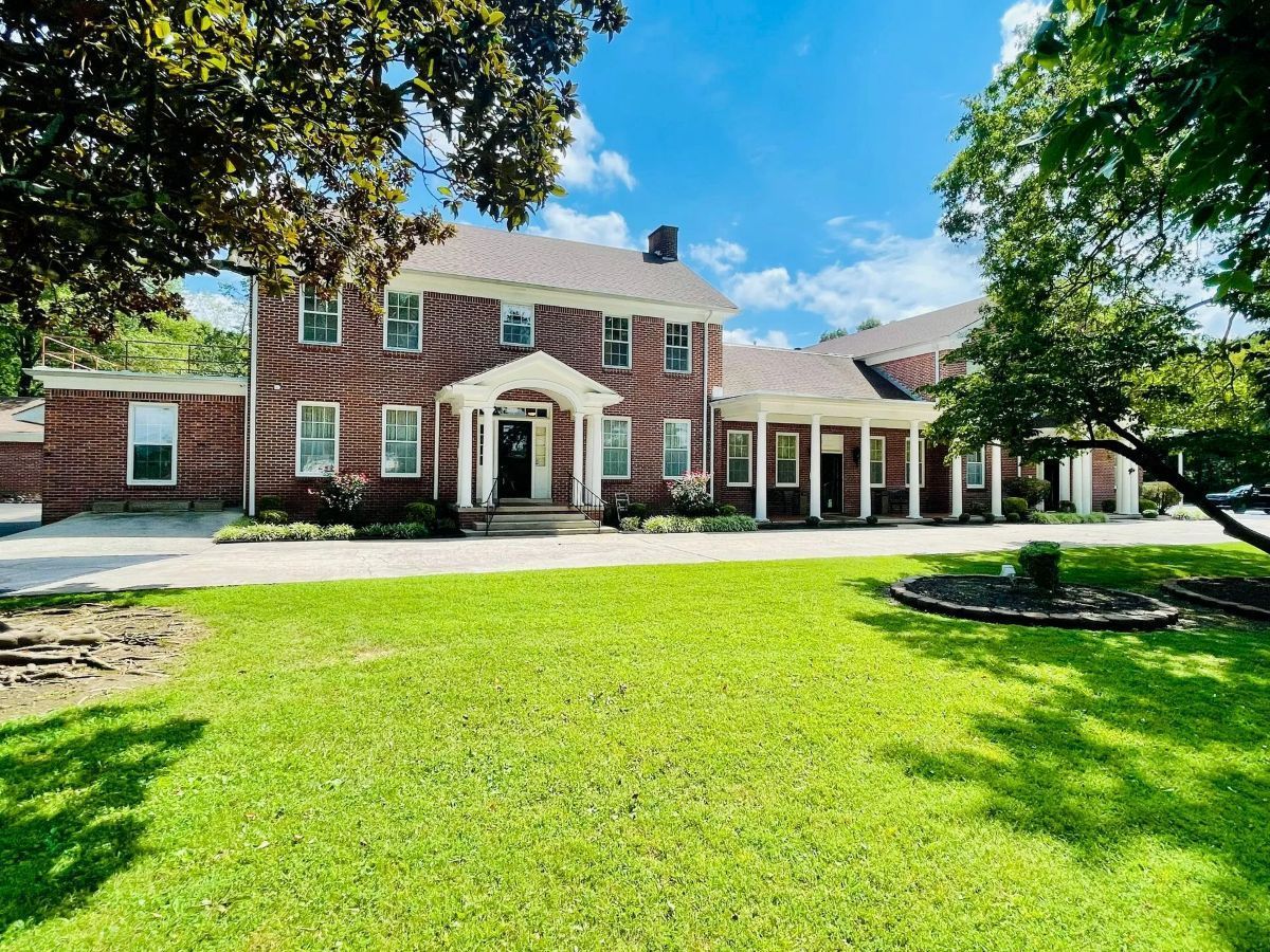 Cream-colored building with red tile roof, American flag, and green lawn.