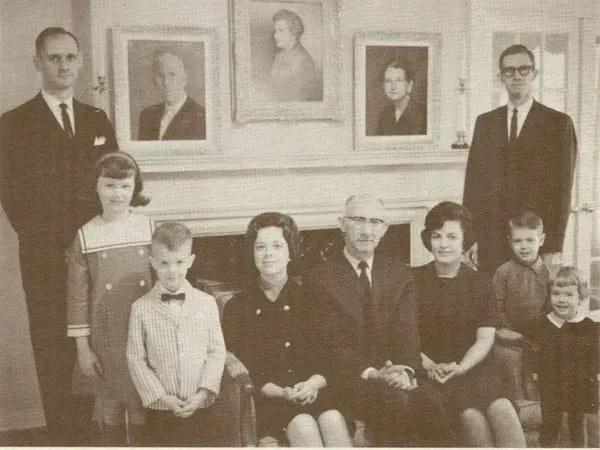 Family portrait in a living room, with eight people posed beneath framed portraits.