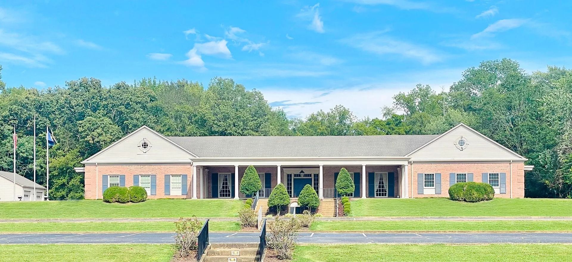 Single-story brick building with white columns and a front lawn under a blue sky